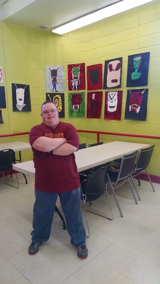 David stands next to his artwork with his arm crossed.